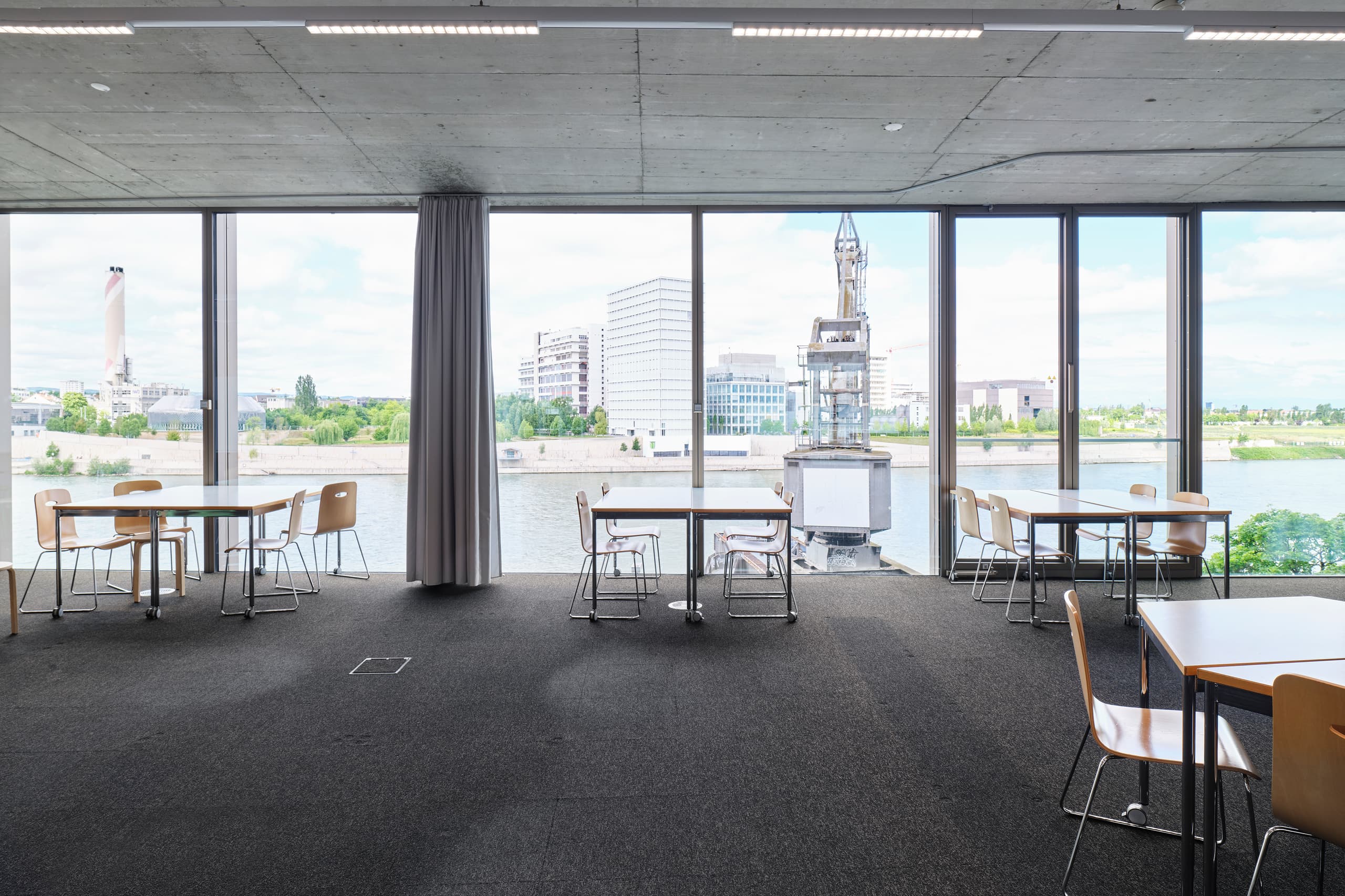 View of a break room in the building WKL-132 in the Klybeck site in Basel with several tables along large windows facing the Rhine river