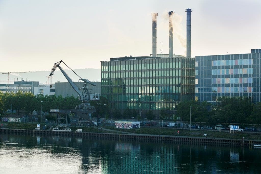 View of the building WKL-132 on the Klybeck site in Basel as seen from the river Rhine with three chimeneys in the background and a crane visible on the left of the building