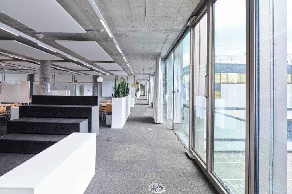 View of a large multifunctional room in the building WKL-132 in the Klybeck site in Basel with large windows on the right and furniture on the left