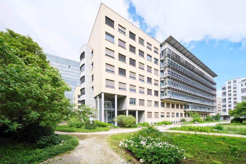 View of the building WKL-136 on the Klybeck site in Basel surrounded by trees and a green lawn with pedestrian walkways
